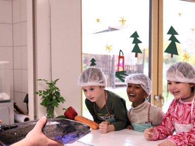 Ein Koch zeigt vier Kindern im Kindergarten einen Lachs.