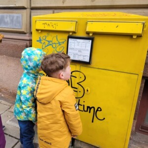 Kinder stehen vor einem gelben Postbriefkasten.
