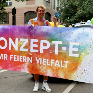 Zwei Erzieher und Frau Weegmann halten das Banner und lächeln in die Kamera beim CSD 24