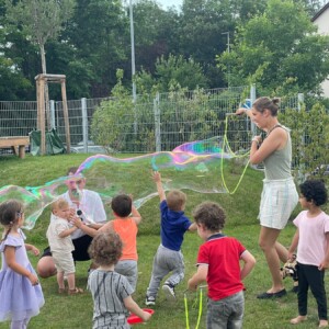 Erzieherin macht im Garten riesige Seifenblasen und die Kinder rennen hinterher