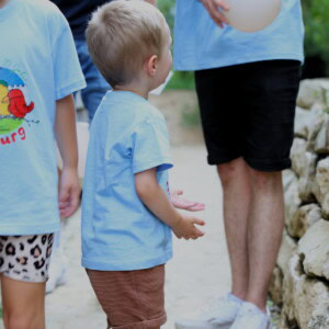 Ein kleiner Junge mit einem hellblauen Finkenburg Tshirt schaut zu seinem Erzieher hoch