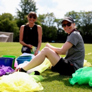 Zwei Frauen sitzen auf dem Sportplatz mit bunten Tüchern und Eimern