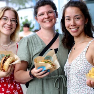 Drei Frauen lächeln in die Kamera bei der Abendveranstaltung des element-i Sommerfests und zeigen ihr Essen