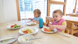 Zwei Kinder sitzen am Tisch und essen Obst und Gemüse